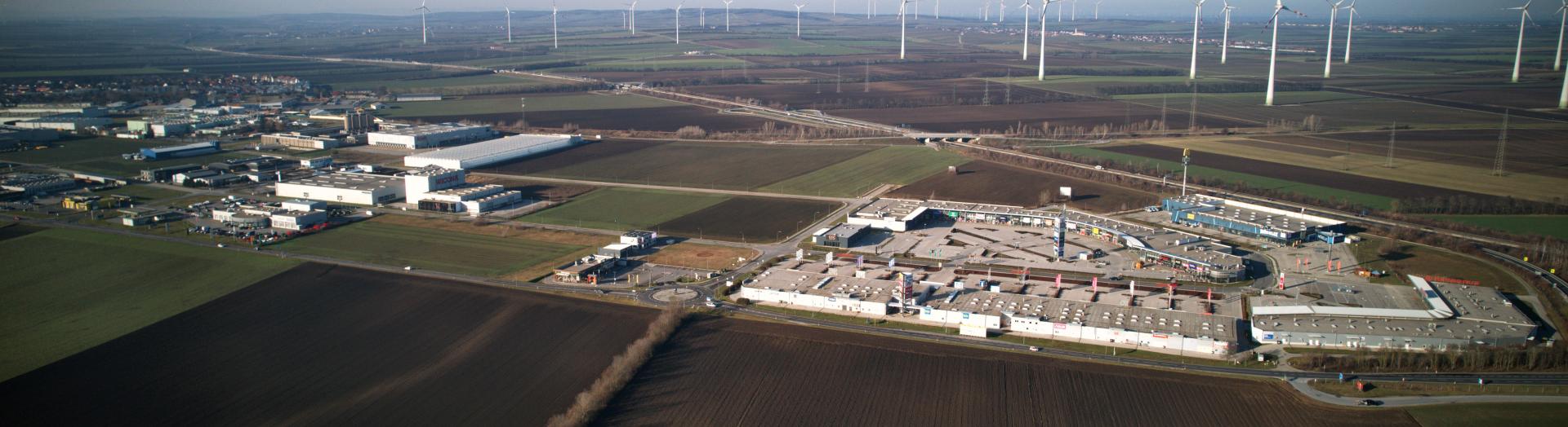 Luftbild Wirtschaftspark mit Fachmarktzentrum umgebenden Feldern und Windrädern im Hintergrund