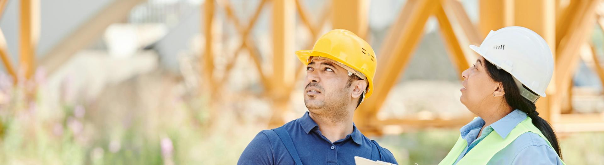 Zwei Personen mit Bauhelmen stehen auf Baustelle