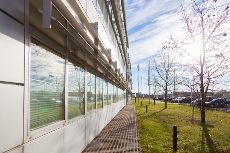 Detailansicht einer Glas-Fassade mit Sonne, Baumreihe und Parkplätzen