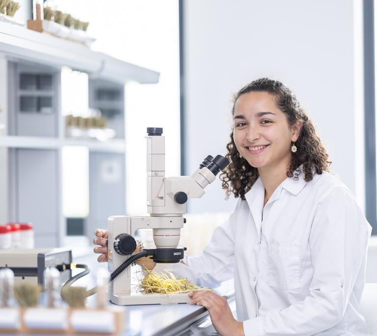 Dame im weißen Labormantel sitzt am Mikroskop 