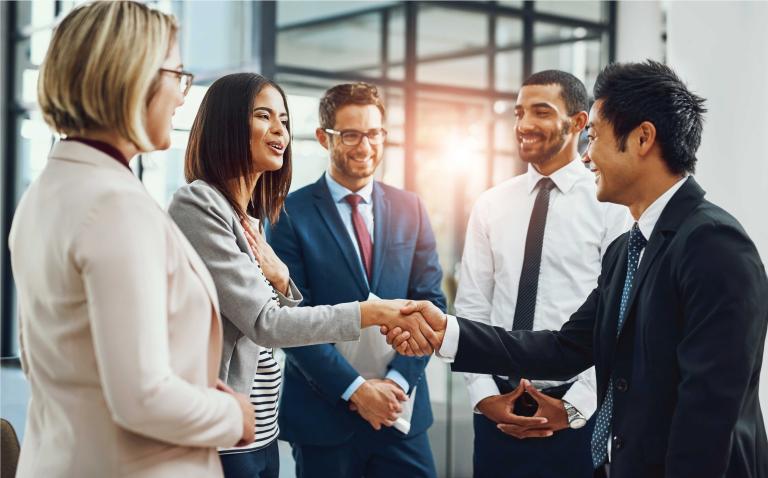 Group of 5 people stand in a circle and lady and man shake hands.