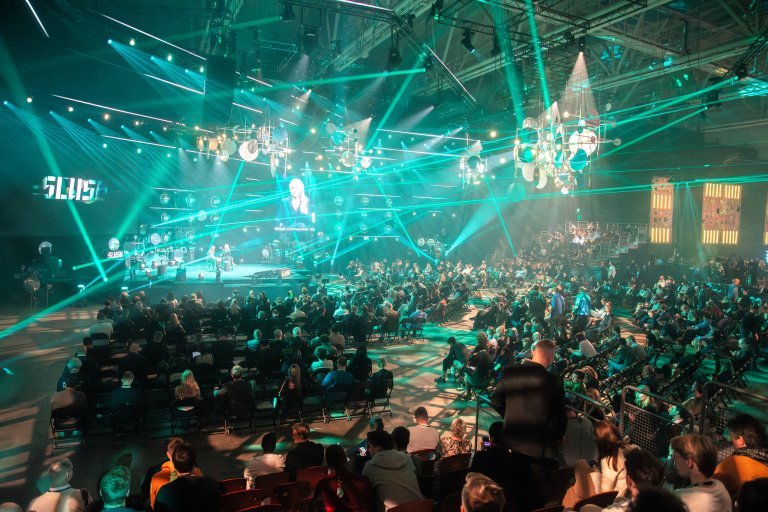 Halle mit Bühne und Vortragenden, Scheinwerfer und einiges Zuseher