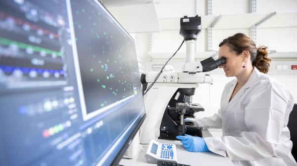 Forscherin beim Mikroskopieren mit großen Bildschirm vom Vordergrund