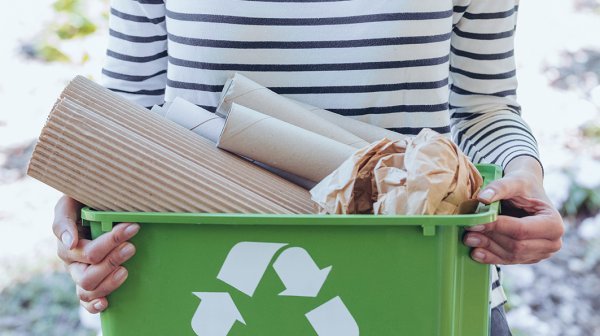 Person mit Aufbewahrungsbox inklusive Kreislaufsymbol gefüllt mit Papier in der Hand