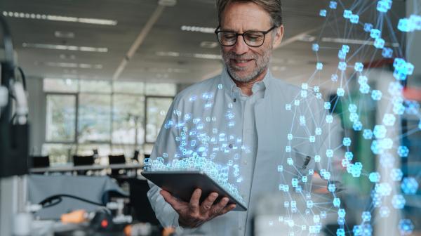 Mann mit weißem Forschungsmantel hält Ipad mit schwebenden Icons in Händen