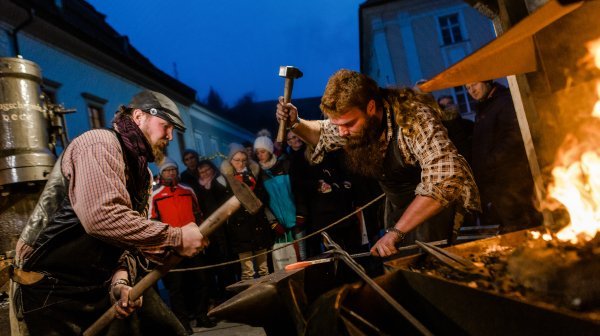 zwei Männer machen Schmiedearbeiten und einige Leute im Hintergrund schauen zu