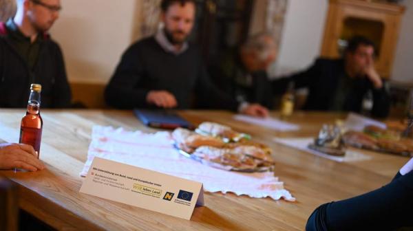 ein Tisch mit einem Aufsteller und im Hintergrund sitzen Personen