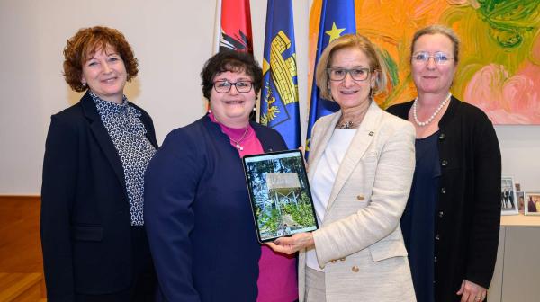 vier Frauen stehen mit Ipad und Bild von Warte St. Oswald nebeneinander und lachen in die Kamera