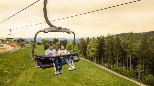 zwei Personen sitzen auf einem Sessellift