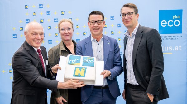 Vier Personen halten vor einer ecoplus Rückwand eine Torte in die Kamera