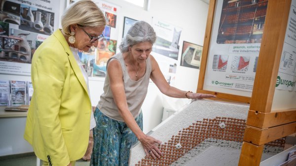 Zwei Frauen beim Betasten von einem Fassadensystem aus glasartigen Vulkangestein