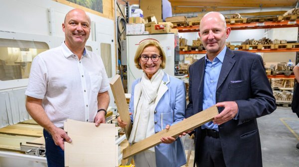 Drei Personen stehen in einer Tischlerei und halten  