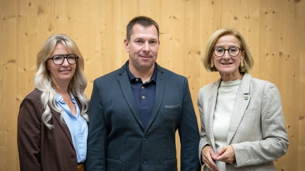 Drei Personen stehen vor einer Holzwand