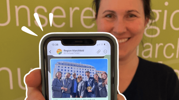 Eine lächelnde Frau steht vor einem grünen Hintergrund mit der Aufschrift „Unsere Region Marchfeld“. 