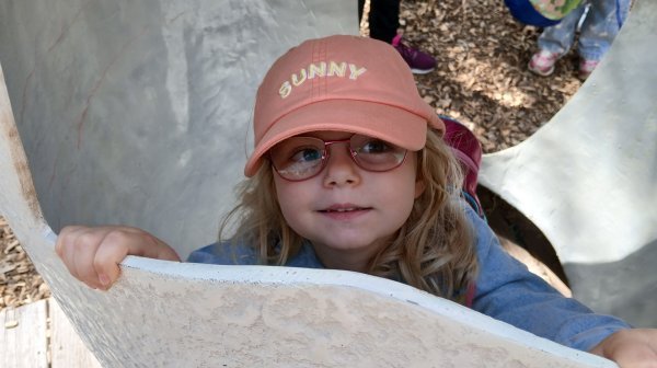 Ein kleines Mädler mit Sonnenkappe auf einem Spielgerät am Spielplatz
