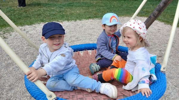 Drei Kindergarten Kinder in einer Korbschaukel auf einem Spielplatz