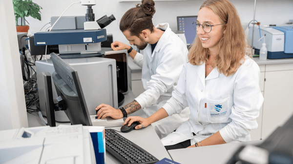 Zwei Personen arbeiten im Labor am Messgerät und werten Daten am Computer aus