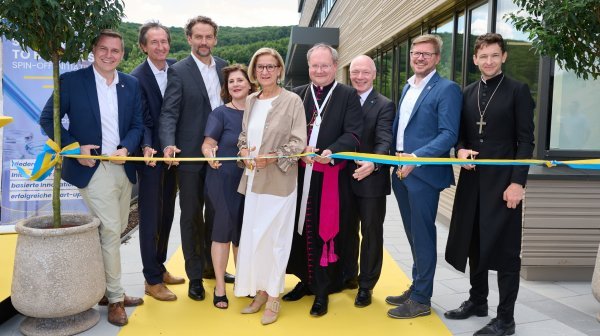 neun Personen stehen nebeneinander und schneiden ein blau-gelbes Band durch