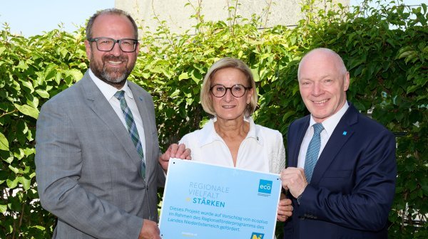 drei Personen stehen nebeneinander und halten ein Schild in der Hand. 