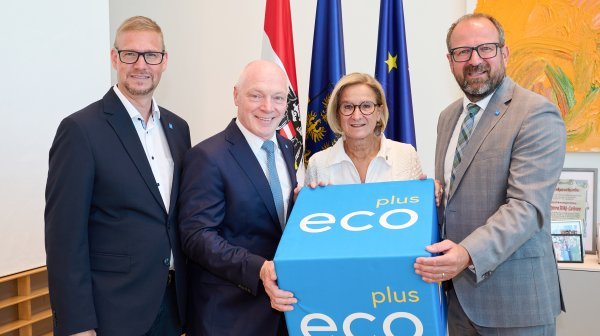 Vier Personen stehen in einer Reihe und halten einen blauen Würfel mit der Aufschrift ecoplus. 