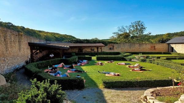 Menschen liegen auf einer Wiese im Kreis auf Matten innerhalb alter Mauern