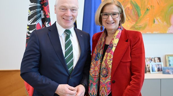 Zwei Personen stehen in einem Büro vor Fahnen und Bildern