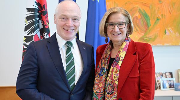 Zwei Personen stehen in einem Büro vor Fahnen und Bildern