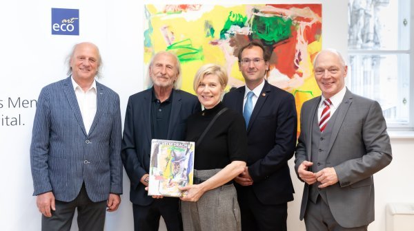 Vier Männer und eine Frau stehen vor einem Gemälde und halten einen Katalog in Händen