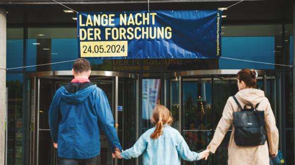 Mädchen hält Eltern an der Hand vorm Eingang zur Langen Nacht der Forschung