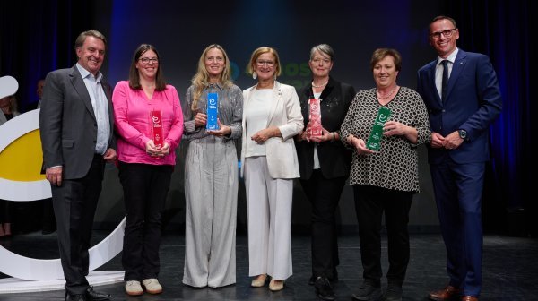 Sieben Leute stehen in einer Reihe mit vier Siegertrophäen
